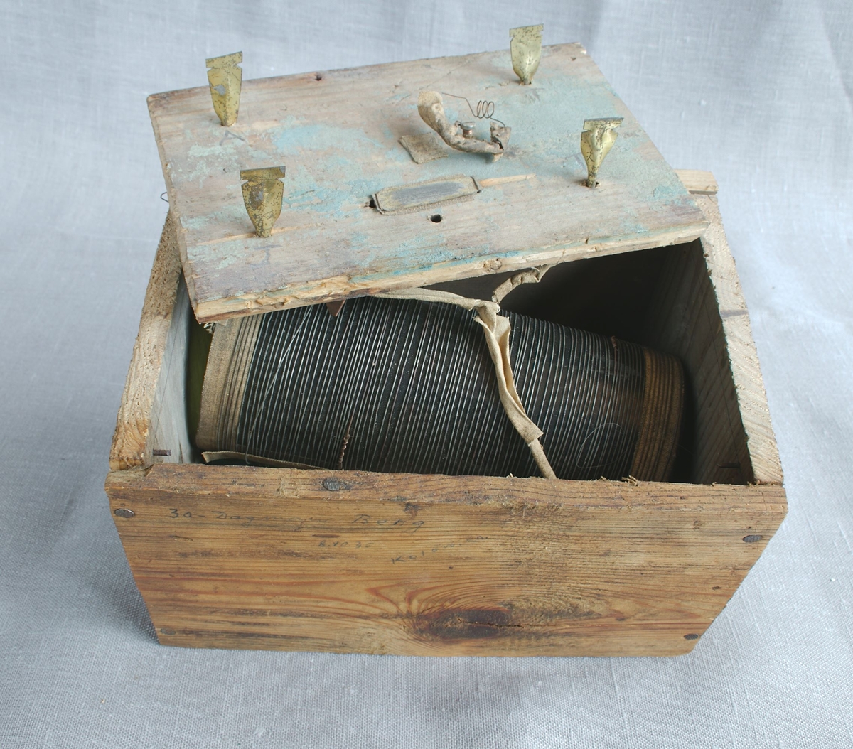 Hjemmelaget radioapparat laget av en trekasse med lokk og ståltråd kveilet opp på en glassylinder. Potteskår, deler av en glassflaske og en ledning medfølger.