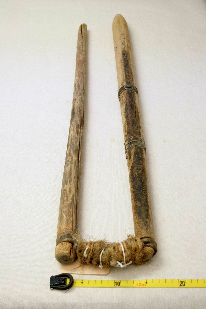 To trestokker som er festet sammen med lærremmer og hampetau, den ene stokken er forsterket med ståltråd.