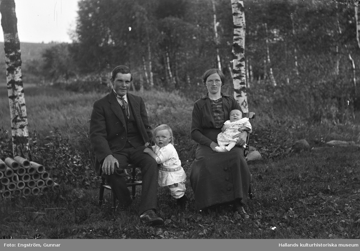Ett ungt par, Klas och Linnea Andersson, sitter med sina små barn utomhus vid ett par björkar på Klingeberg, Hästhagen (Danskens) i Sällstorp. Pojken vid Klas heter Gunnar Sigurd och bebisens namn är Elin Viola, född i juli 1916, så det ger bildens datering. Till vänster ligger smala rör travade. (Se även bildnr GEA006)