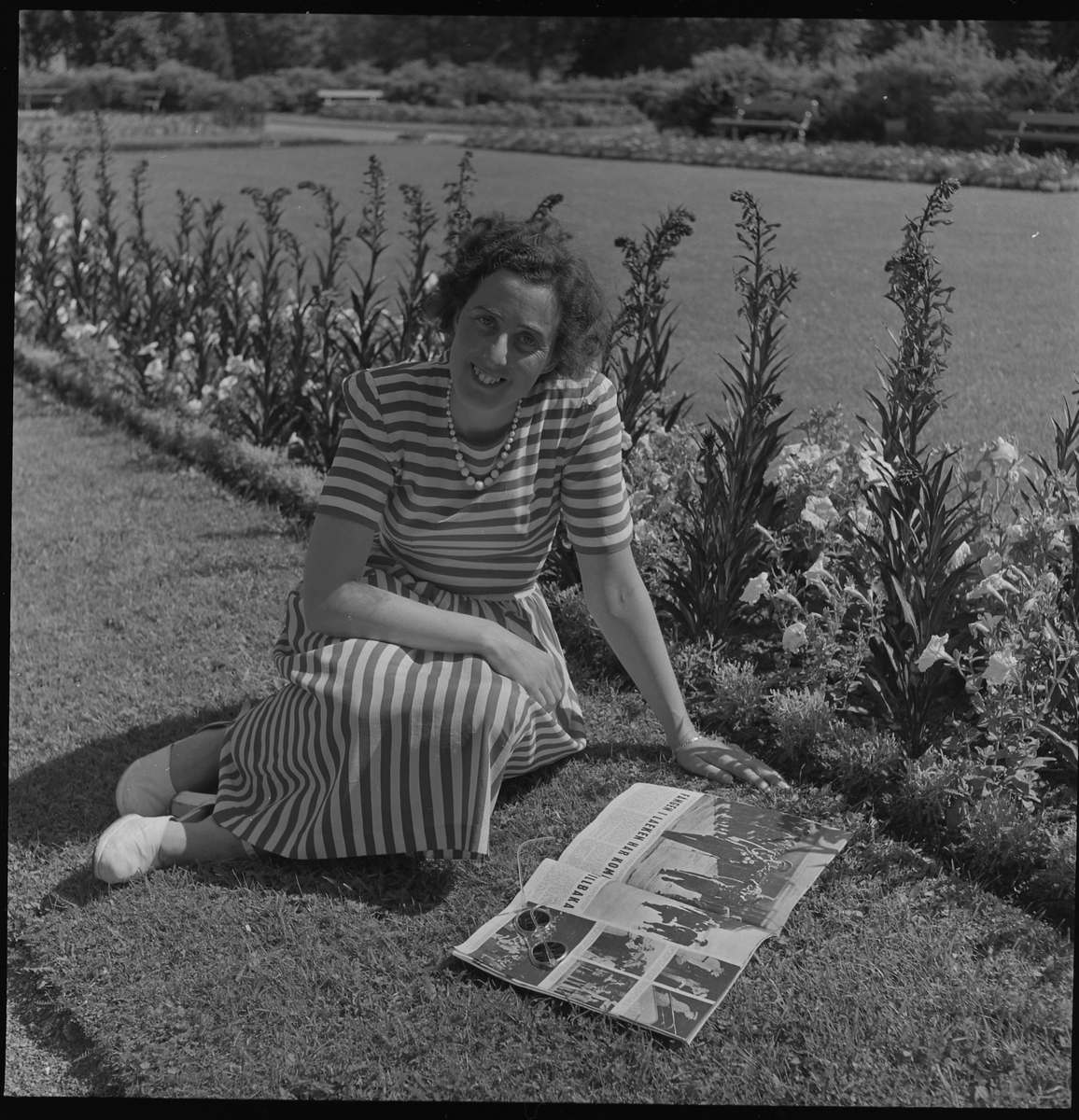 Kerstin Åsén sitter i gräset och läser en tidning i Plantaget.
