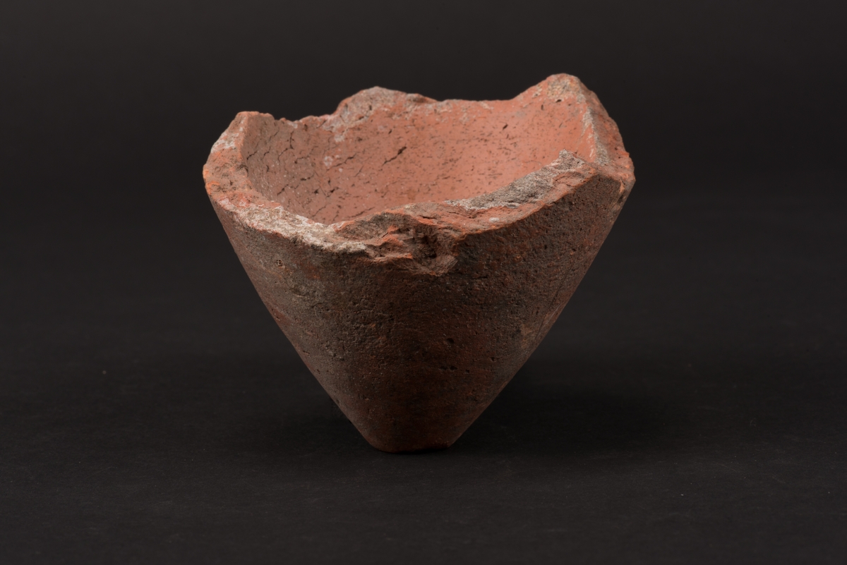 Fragment av en sockertoppsform i lergods. Fragmentet består av den koniska spetsen av formen med ett hål för sirapen att rinna ut.