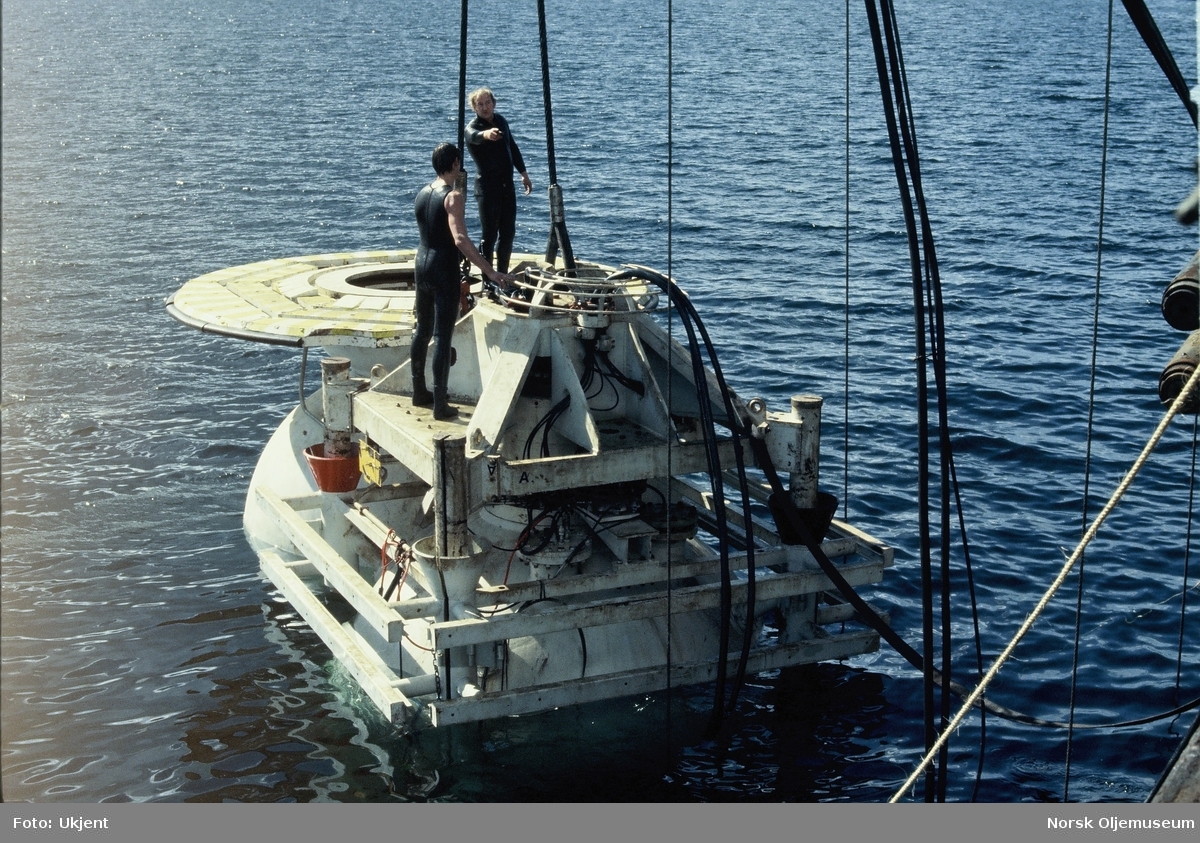 Moduler for et undervannsanlegg monteres utenfor kanten fra en båt eller lekter. Menn i våtdrakt arbeider oppå modulene.