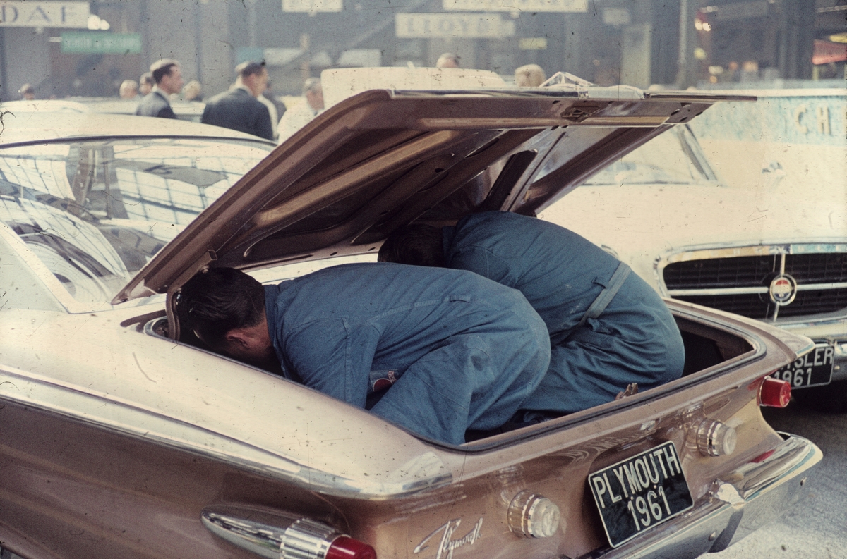 Foto fra en bilmesse i Frankrike. To mekanikerejobber i bagasjerommet på en Plymouth 1961-modell.