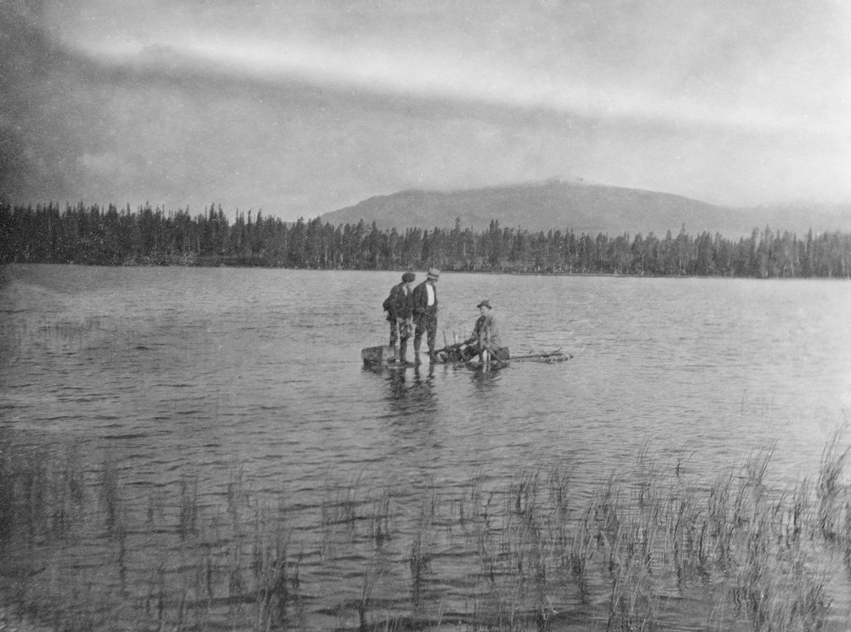 Tre menn på flåte på innsjø omgitt av granskog.  I underteksten er vatnet kalt for "Fiskeløisa". 