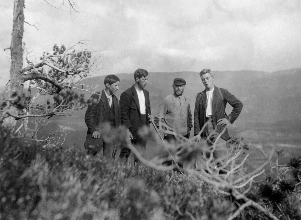 Fire menn, antakelig tre skogtaksatorer med kjentmann på en lyng- og furubevokst bakkekam i Byaskogen i Grong.  I bakgrunnen skimtes et dalføre med skog og vassdrag. 