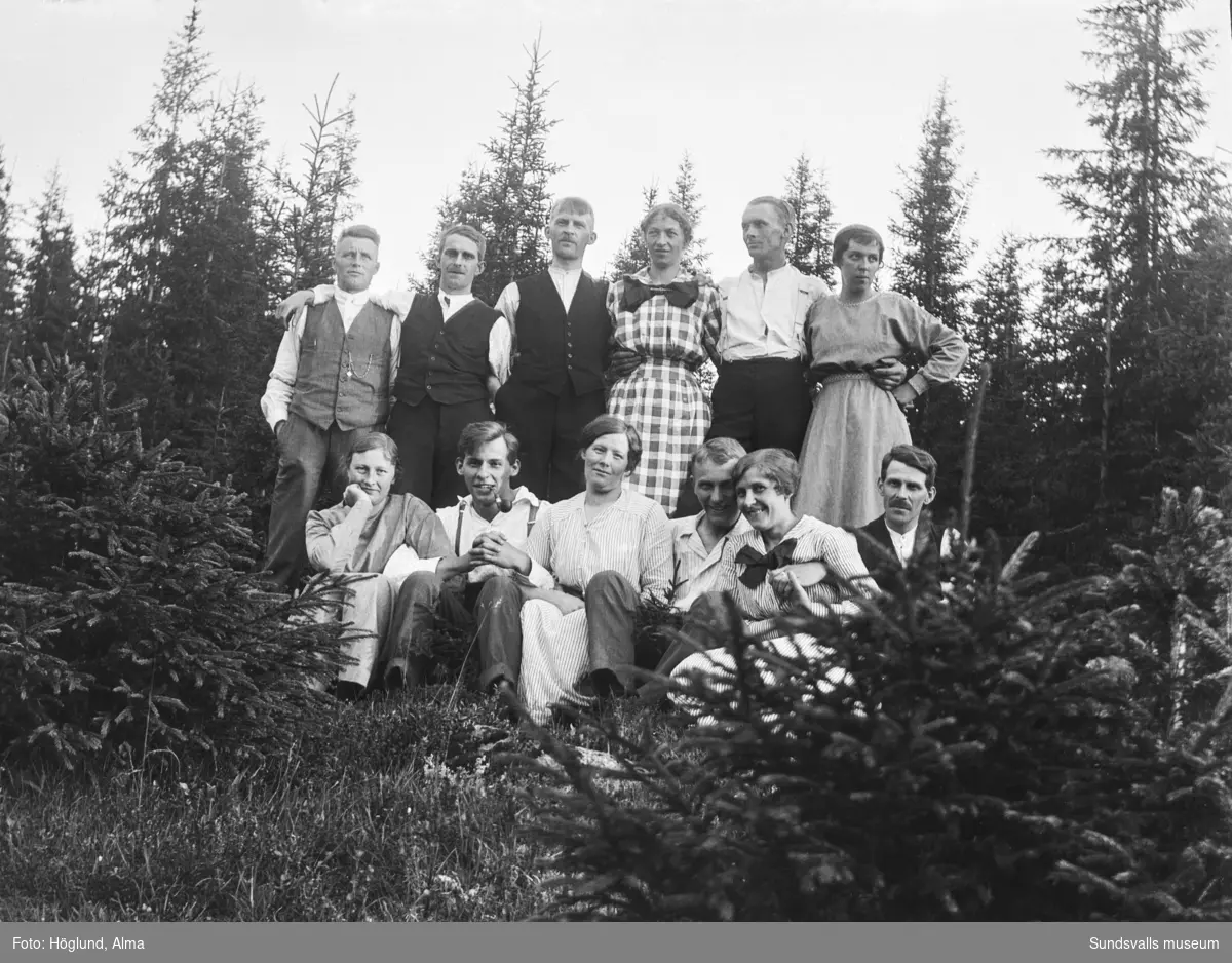 Två gruppbilder med tolv personer i en skogsbackeSamma personer på båda bilderna förutom nummer fyra längst fram. På bild nummer två sitter där Helmer Höglund, övriga är oidentifierade.
