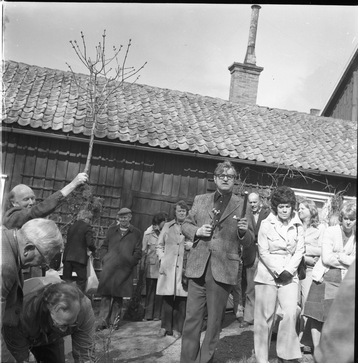 Auktionsutroparen John Karlsson i en folksamling. Bakom honom till höger skymtar Elof Carlsson i Röttle. En man till vänster håller upp en trädplanta.