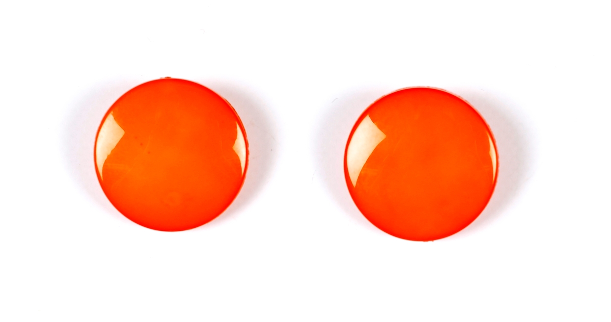 Et par oransje sirkelformede plastøredobber med  klips i samme fargede plast på baksiden.