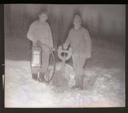 Fotografi av to menn står i snøen som arbeider med noen rør 
