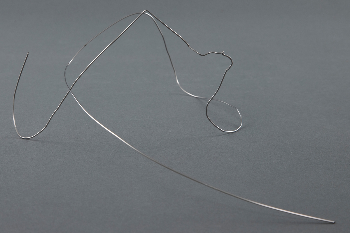 Hodesmykke som består av en tynn ståltråd som er formet i en lang bue, videre i mindre, uregelmessige buktninger og ender i en stor "krok". Smykket er beregnet til å føres fra, for eksempel, øret via nesen over øyelokket.