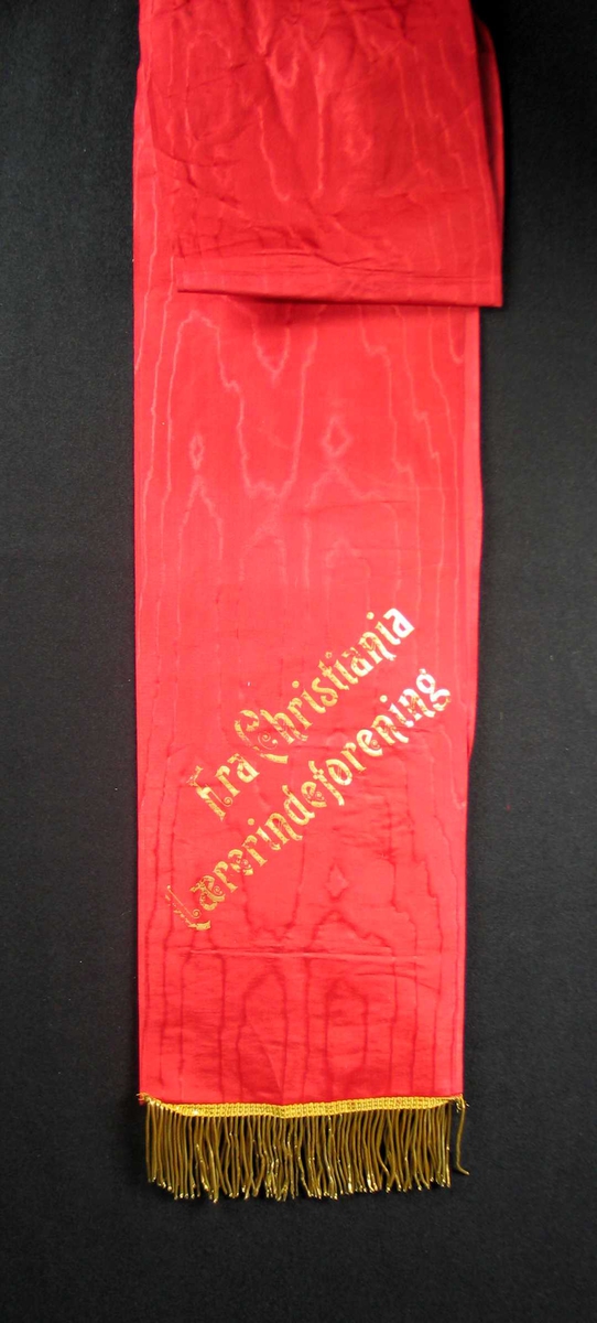 Begravelsessløyfe i rød silke med tekst og frynser i gull.