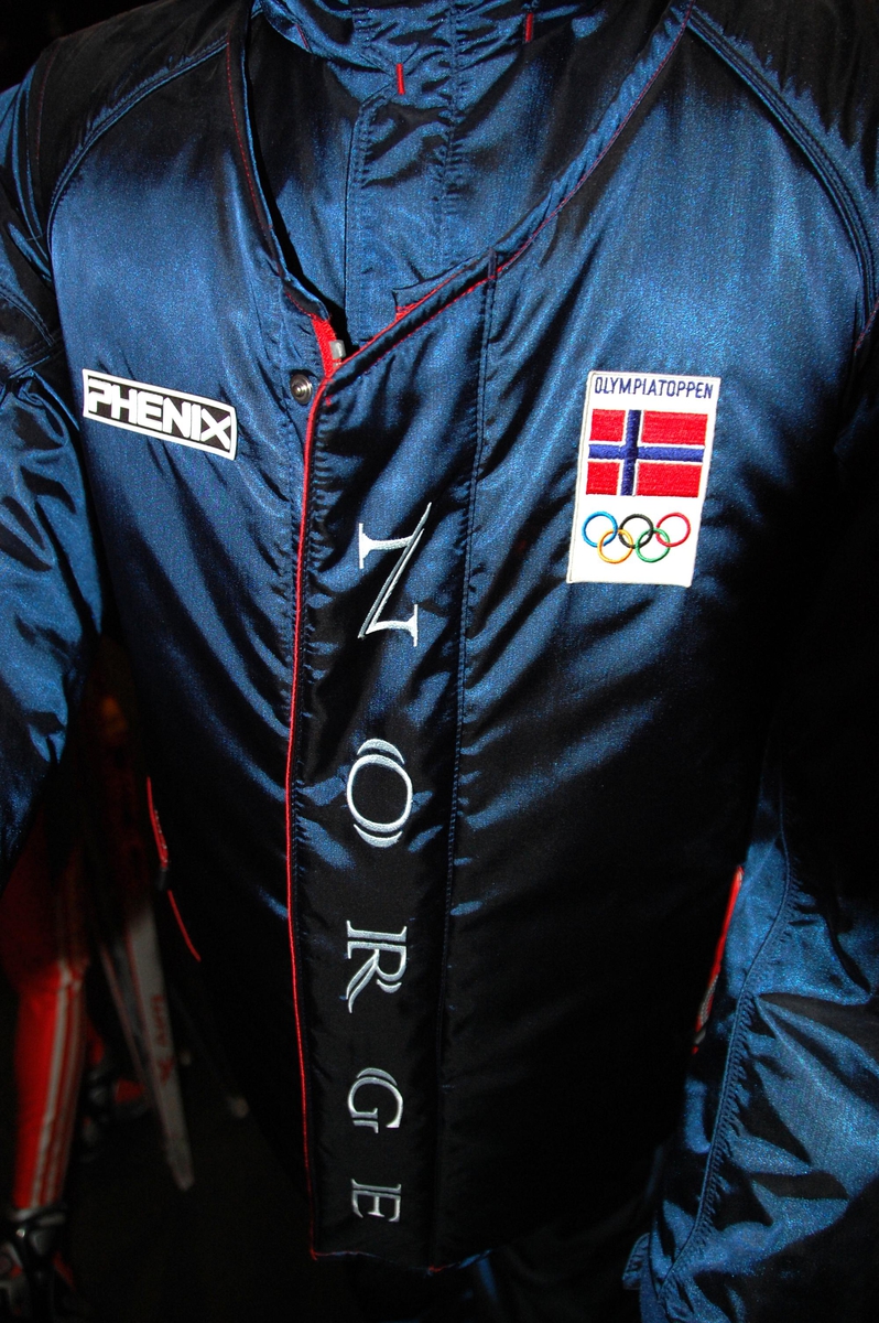Blå vest med motiv på ryggen av et vikingskip med et norsk og et olympisk flagg på masten.