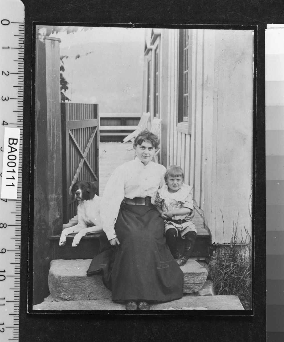 Fotografi av mor med sønn og hund på verandatrinnet en sommerdag.