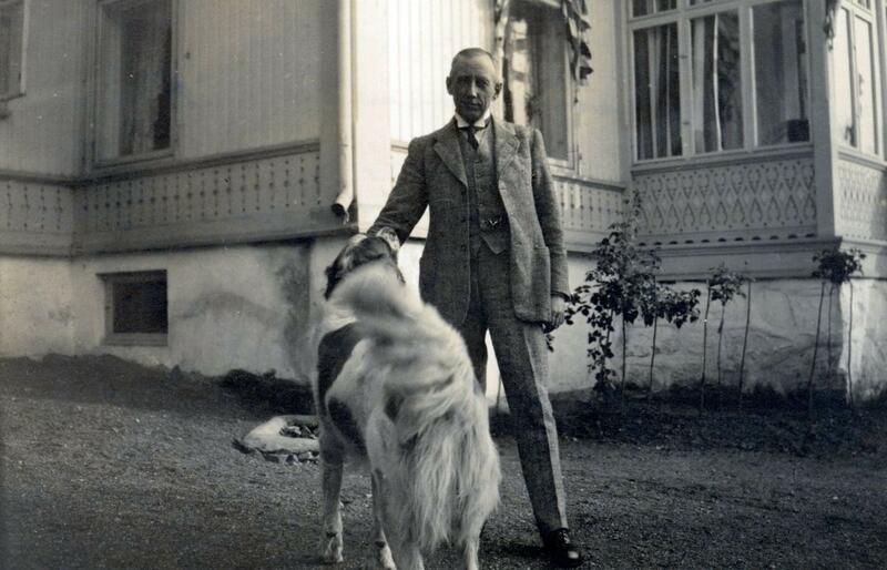 Mann står sammen med en hund foran hus. (Foto/Photo)