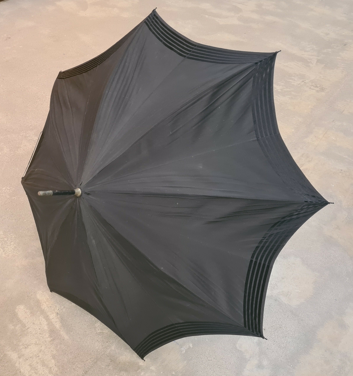Parasoll i svart tyg. Vid skaftet hänger två tofsar.

Ingår i en samling av nio olika parasoller med olika utseende och modell.