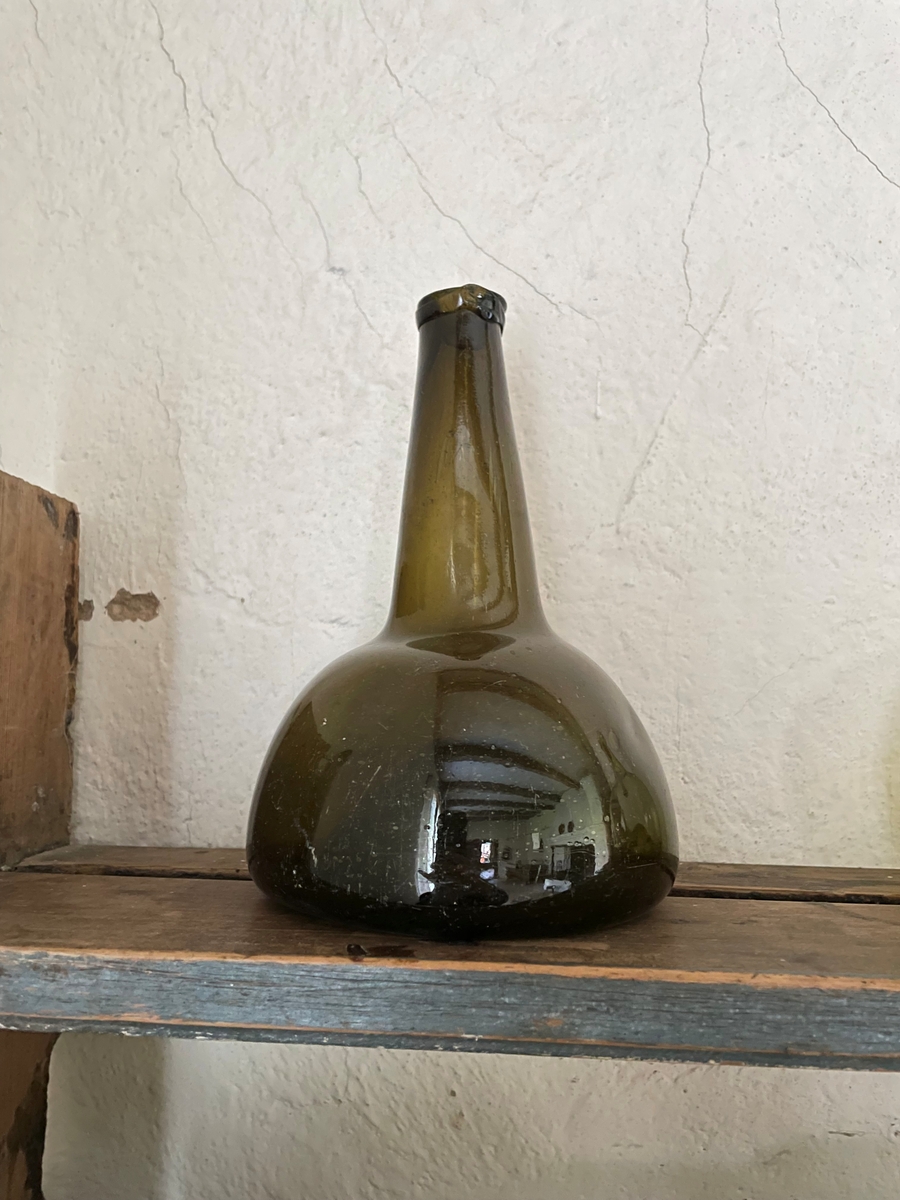 Flaska av grönbrunt glas, långhalsad med botten uppskjuten.