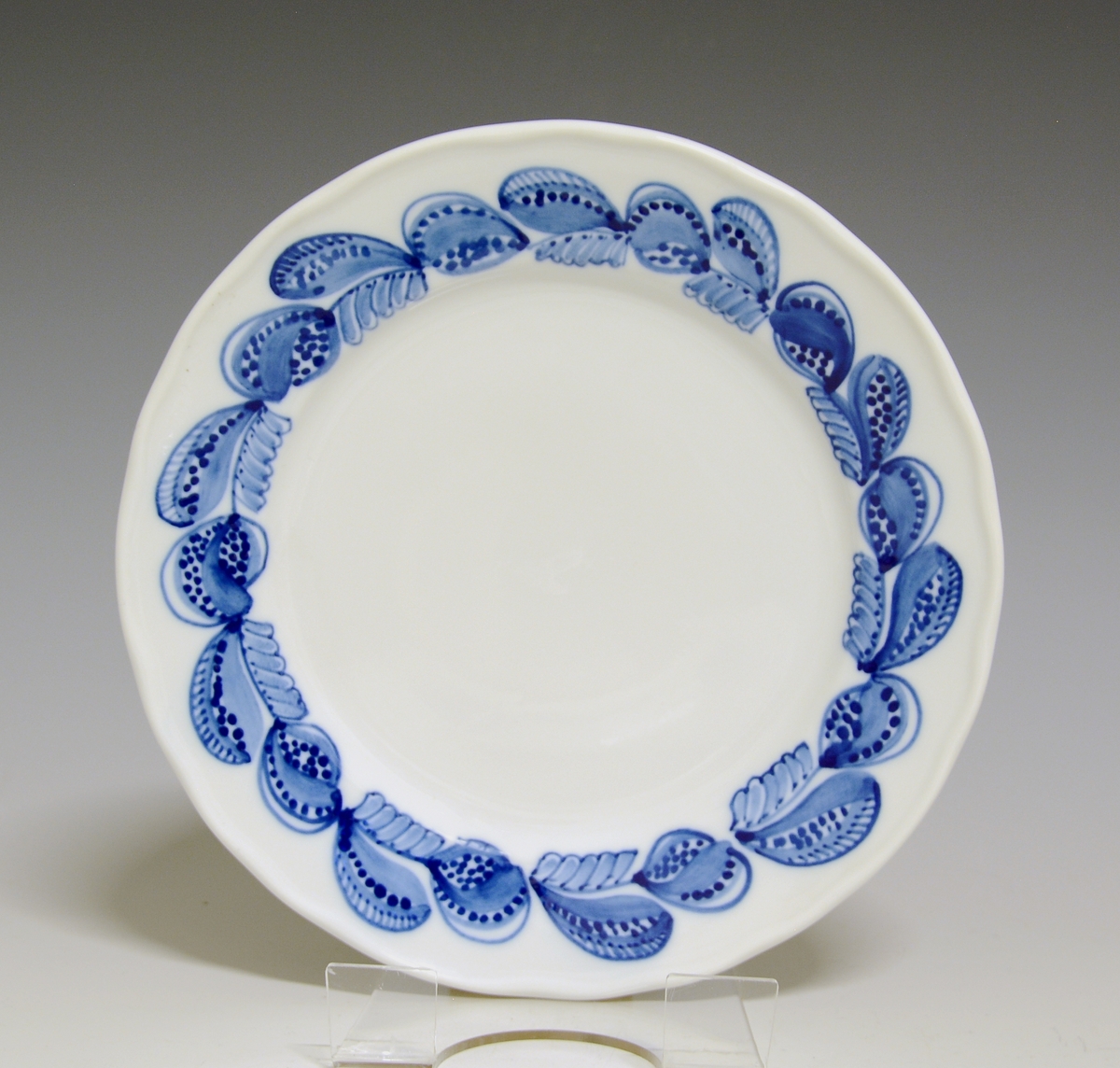 Liten tallerken av porselen. Hvit glasur. Håndmalt underglasurdekor i blått på fanen 
Modell: Victoria, 1800