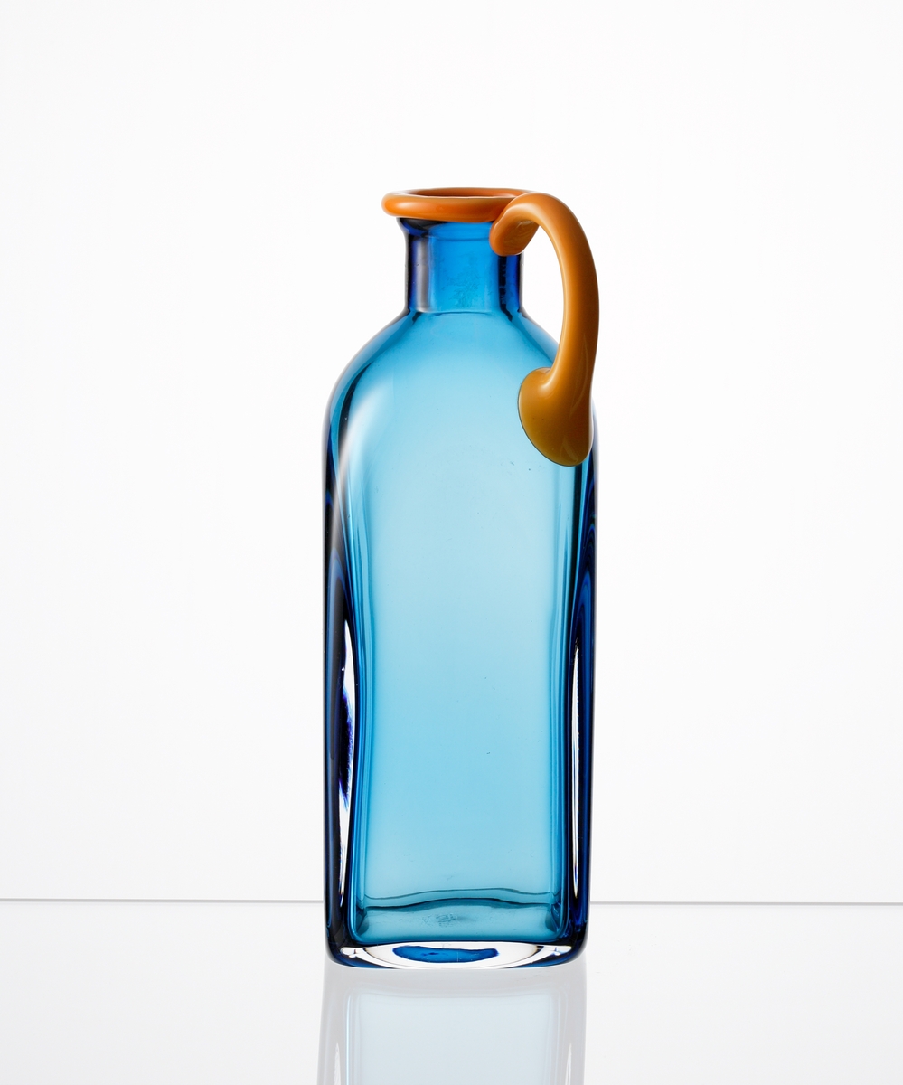 Formgiven av Erika Lagerbielke. Fyrkantig flaska "Confetti" i ljusblått underfång, med orange mynning och hänkel.
