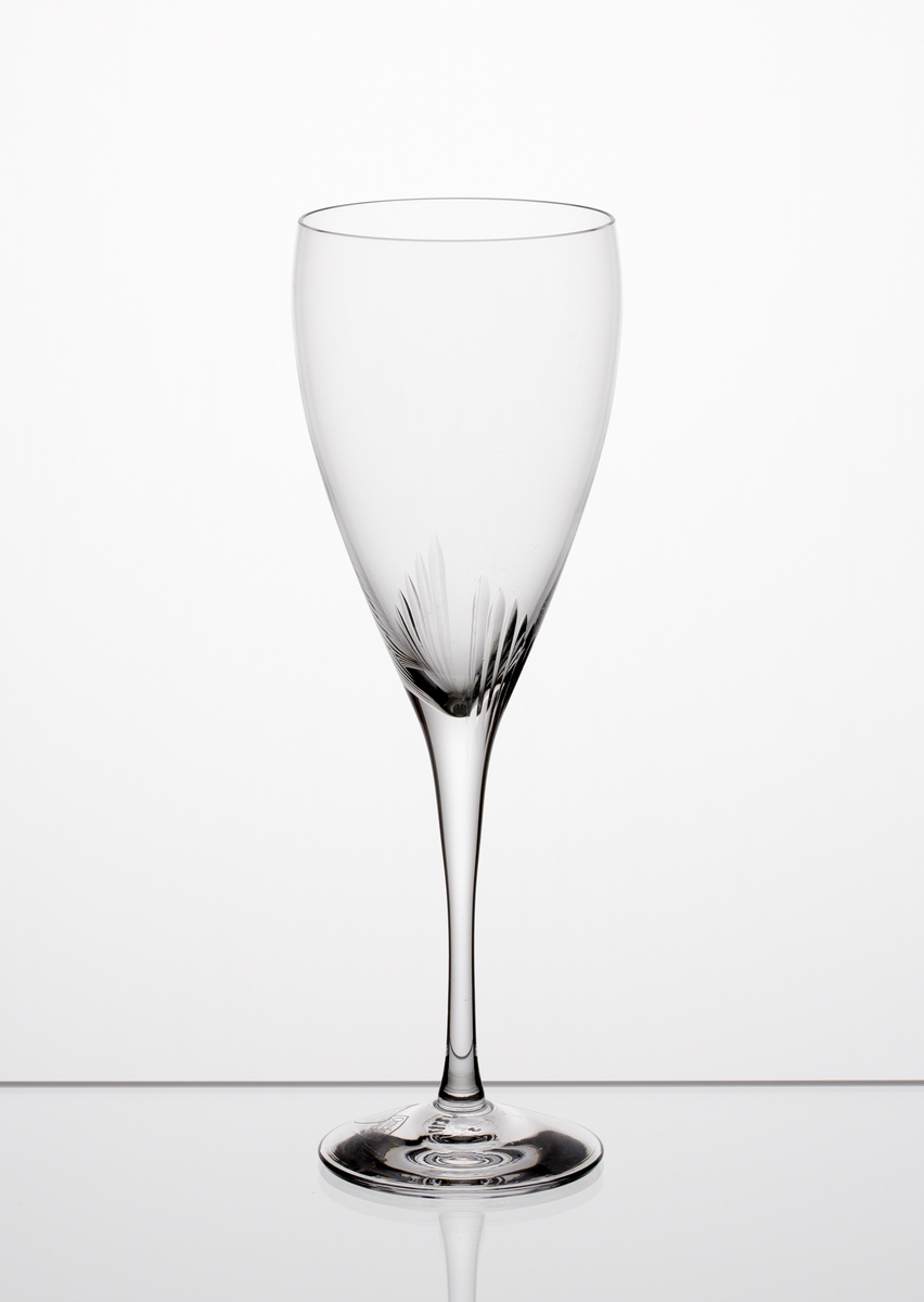 Formgiven av Erika Lagerbielke. Ölglas med nio plus nio stående skär placerade där skålen övergår i ben. Genomskinlig etikett med orre och text i silver.

