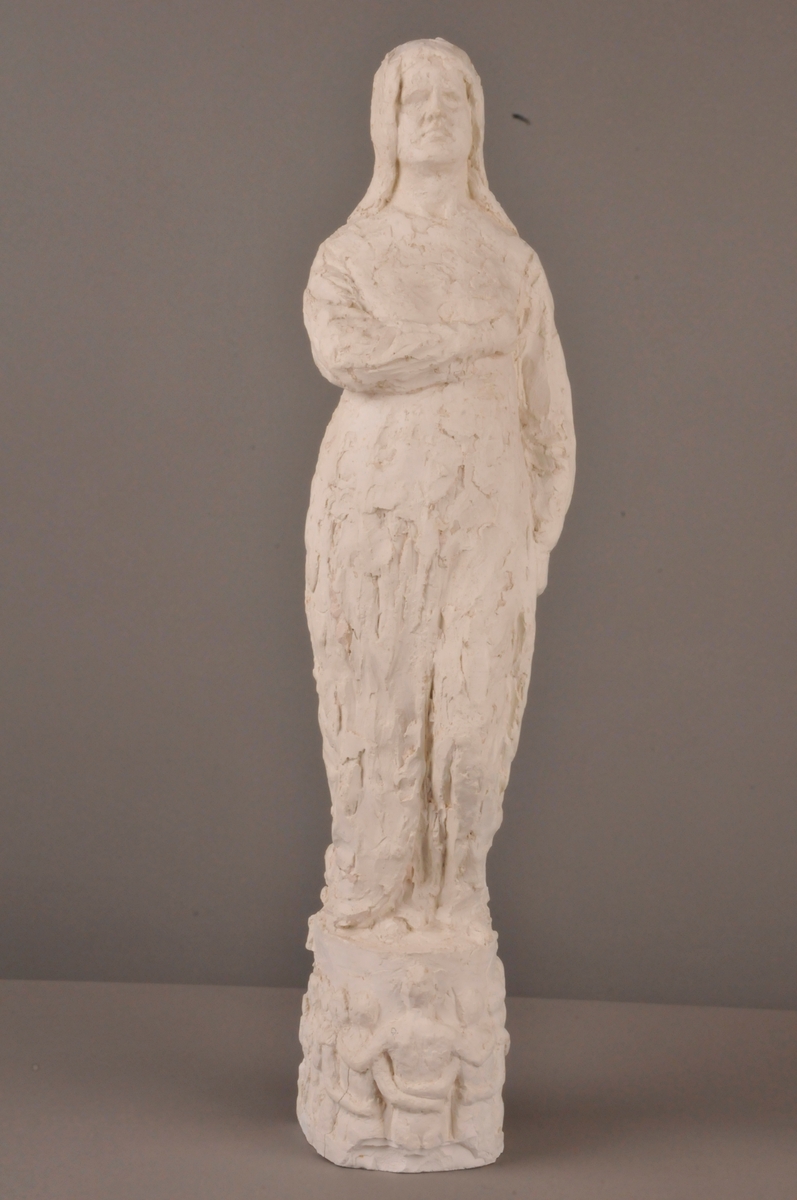 Figur med høgre hand lagt over brystet, venstre heng langs sida. På sokkel: Figurar som held kvarandre i hendane.