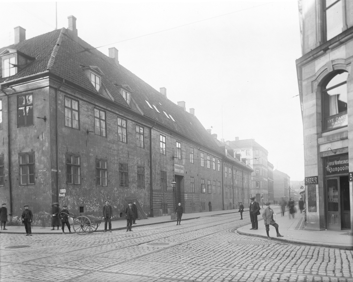 Generalitetsgården/Departementsgården i Dronningens gate 15 i Oslo. Noen menn har stilt seg opp i gatekrysset. Gården ble revet 1916 og gjenoppbygget på Folkemuseet i 1928. Fotografert 1912.