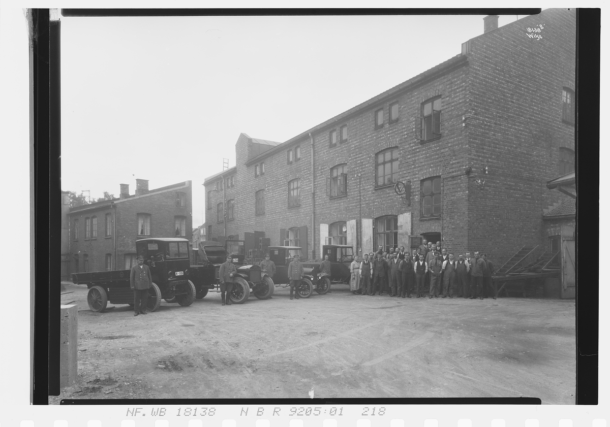 Ansatte, sjåfører og biler står utenfor bygning til Vinmonopolet. Fotografert 1924.