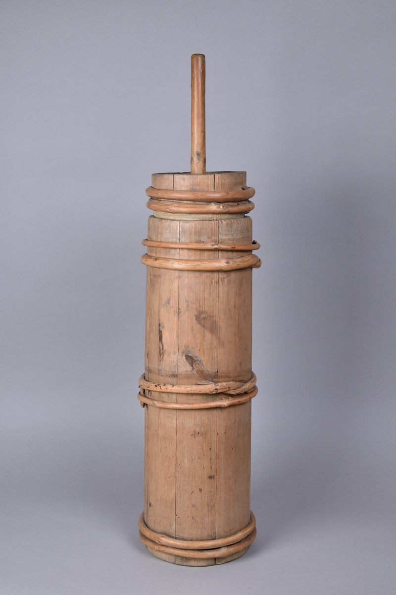 Smörkärna tillverkad i furu och en, laggad. Cylinderformad med åtta band av vidjor. Med lock, samt stöt med rundat skaft och korsformad botten.  