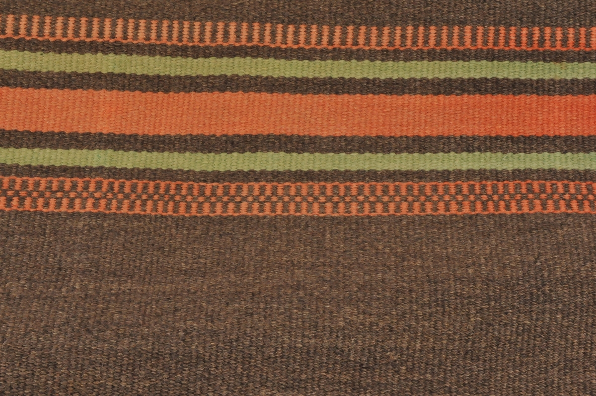 Teppe vove i  med kjeringtann, striper i ulike bredder og fargar. Renning av bomull 26/10,ull i innslag. Teppet er sydd saman på midten. Falda for hand på kortsidene.