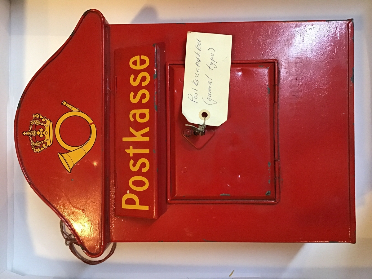 Raud postkasse, med postens logo, for levering av brevpost. Raude postkassar var låst, her ser me nøkkelen står i, og  dei vart regelmessig tømde av postbudet.