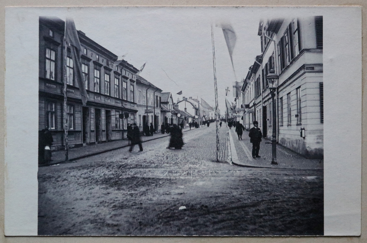 Motivet på detta kort är nedre Kungsgatan, Enköping. Fotot är taget från Ågatan/Stora bron upp mot centrum. Med tanke på de många flaggstängerna som kan ses uppsatta längs gatan skulle fotot kunna vara taget omkring tiden för invigandet av Enköping-Heby-Runhällen (EHR) järnvägsbana i november 1906, då bl.a. kronprins Gustaf, sedermera kung Gustaf V, var på besök i staden. (Jämför vykort EM16069_14).

Vykortet är inklistrat i vykortsalbum nr. EM06774:b.