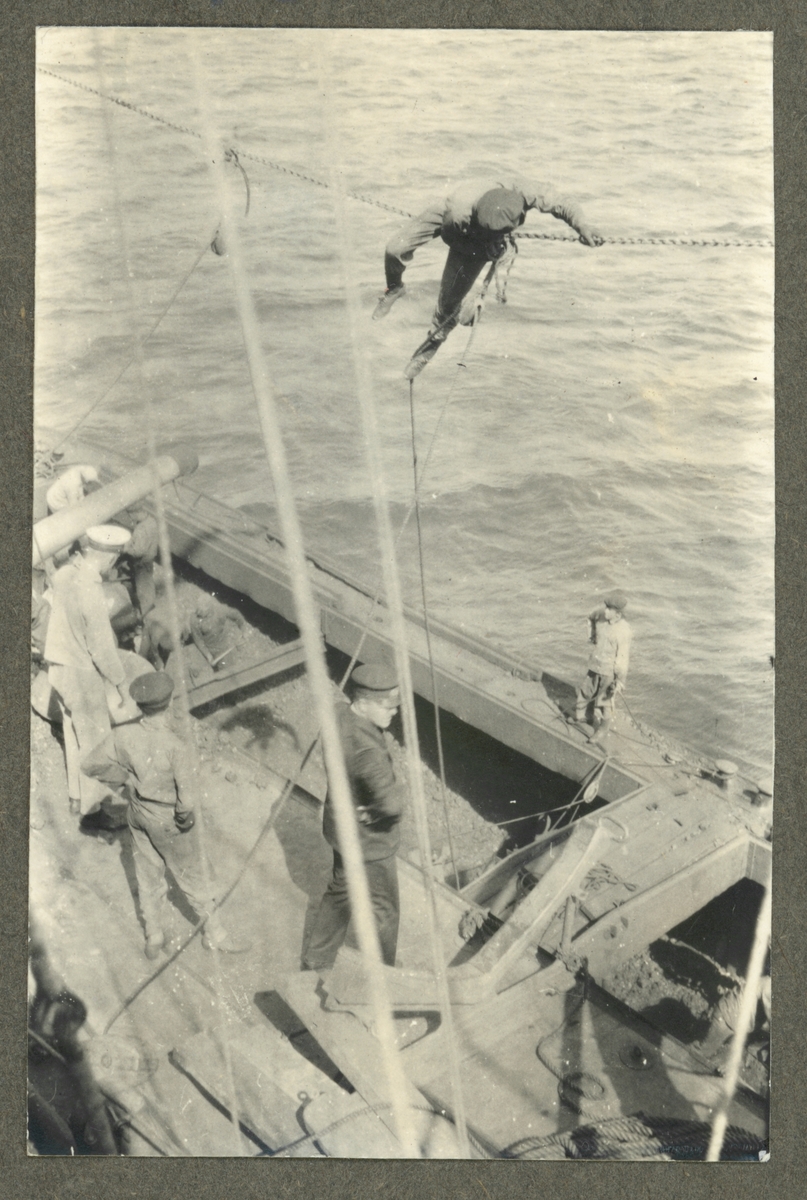 Bilden visar arbeten under kolningen av Fylgia. En man sitter på den rep högt över pråmen och förbereder en lyftanordning.