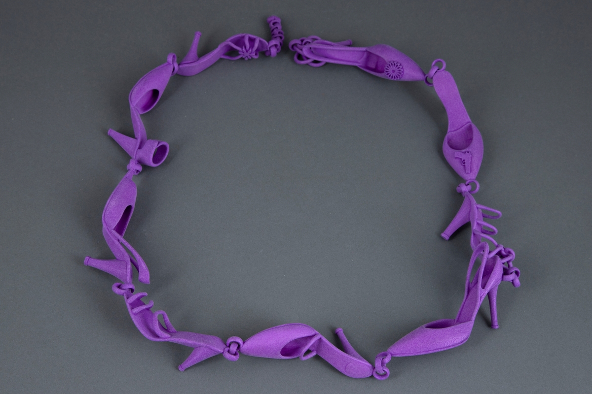 Halssmykke satt sammen av ni ulike høyhælte miniatyr-damesko som er leddet sammen med små ringer. Smykket er utført i glass og trukket med fiolett nylon. Låsen består av et hjerteformet ledd som tres gjennom en ring.