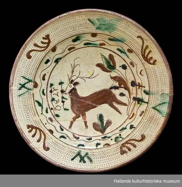 Fat av glaserat lergods/rödgods. Dekorerad med en lekfullt skuttande hjort omgiven av växtslingor och geometriska mönster. Märkt: 1780.
