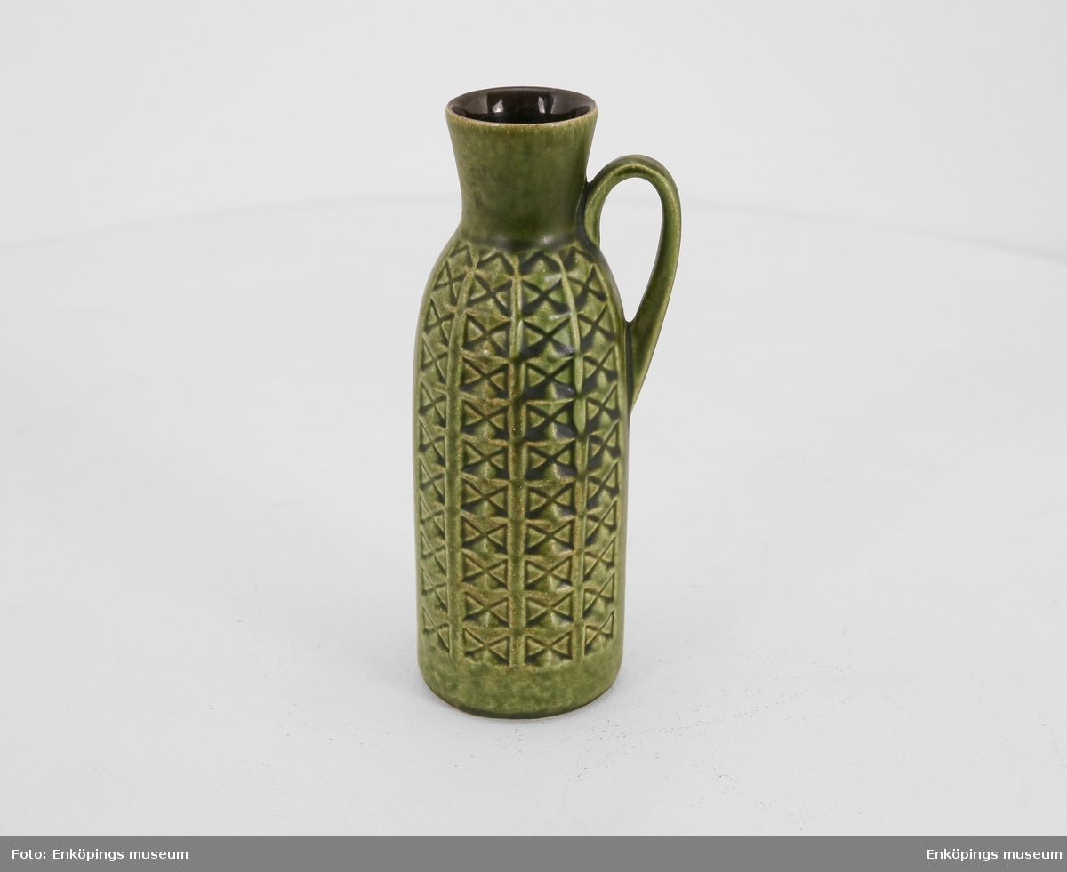 Grön vas tillverkad av det Västtyska företaget Bay. I botten av vasen finns märkningen "W.- GERMANY 234- 20". Vasen har en hänkel (handtag) och själva designen är smal. Mönstret utgörs av små kors inuti rektanglar som staplas på rad från botten av vasen upp till toppen. Vasen är från 50-/60- talet.