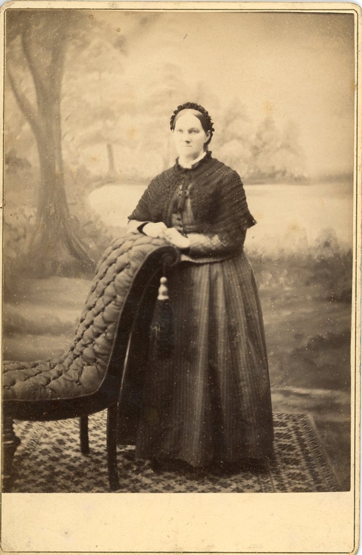 Kabinettsfotografi av en kvinna som står vilande mot en stolsrygg.