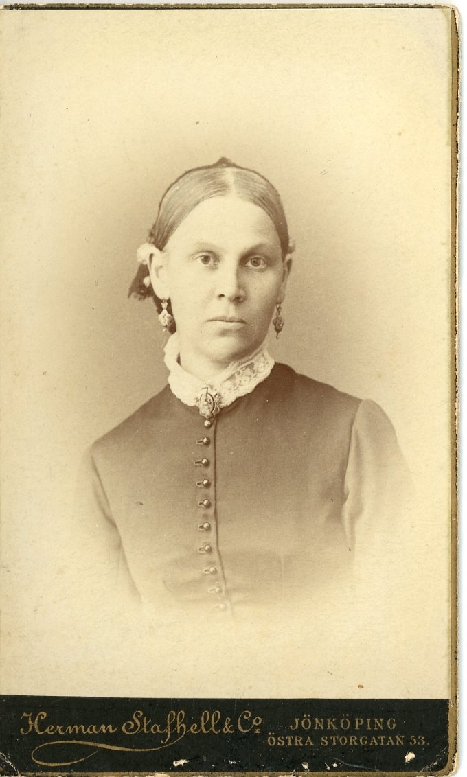 Kabinettsfotografi av en kvinna med örhängen och en brosch vid halsen.