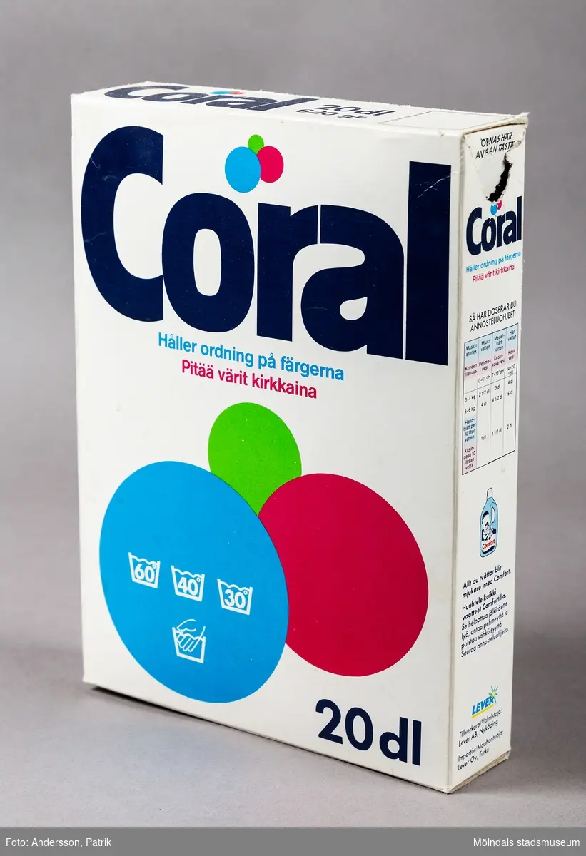 En vit rektangulär kartong som innehåller tvättmedel av märket Coral. Kartongens vita framsida är dominerad av en svart text med namnet Coral och tre färgstarka cirklar. Cirklarna har olika storlek och utmärks av stark färgintensitet i blått, grönt och rosa.
Tillverkaren Lever var ett svenskt bolag som tidigare lanserads under namnet Sunlight AB. Tvättmedlet tillverkades förmodligen mellan 1987-1992 innan produktionen för Lever lades ned.