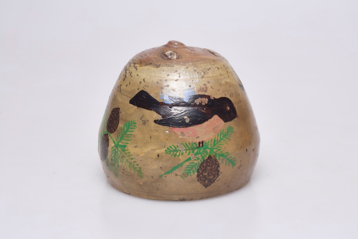 Sparebøssen er dekorert med granbar, kongler og en fugl. Et ansikt preger sparebøssen på oversiden. Munnen fungerer som åpning til å putte penger i.