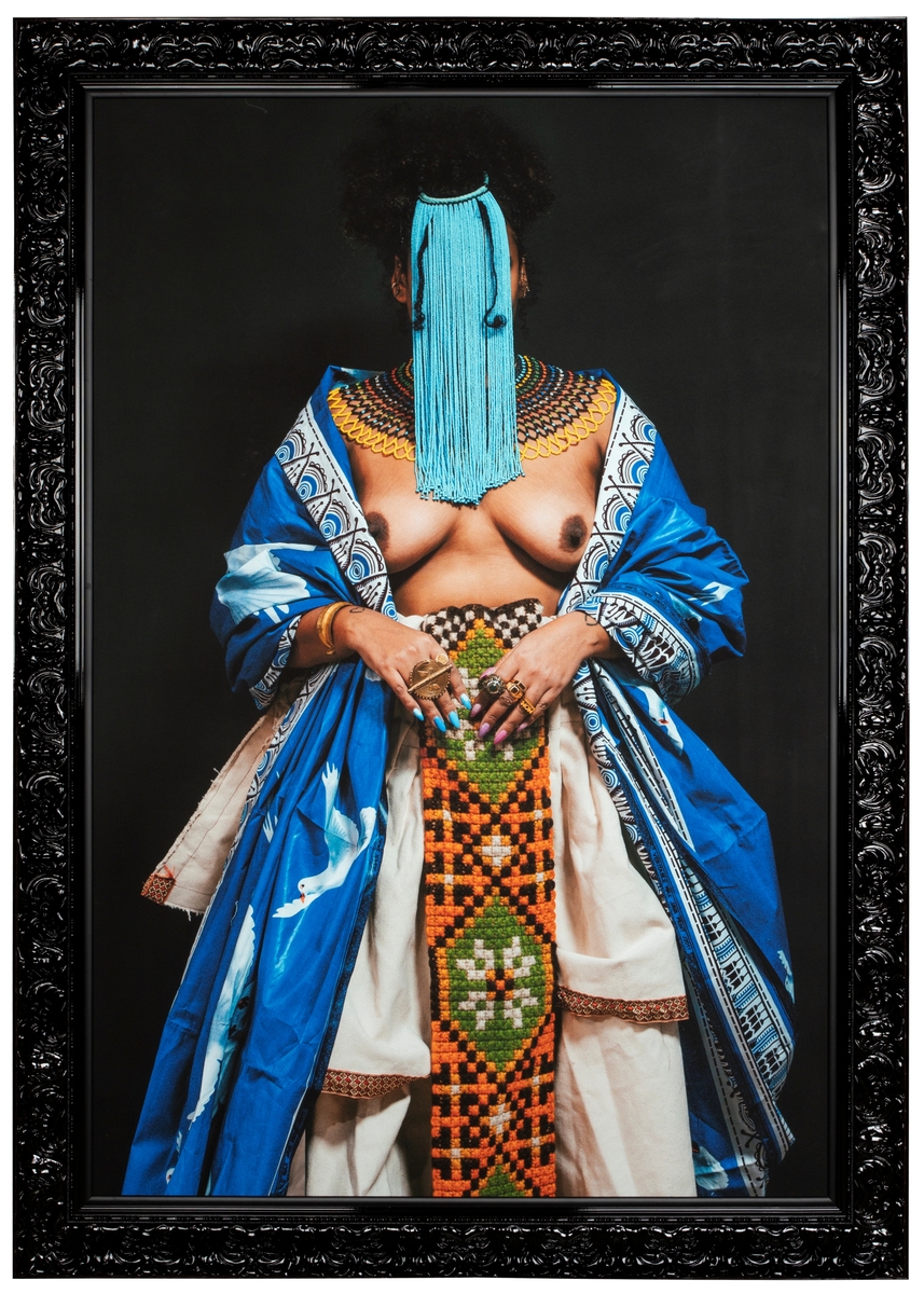 Stort rektangulært fotografi av kvinne kledd i ulike plagg med ulike kulturelle opphav. Kvinnens ansikt er skjult bak en maske av tråder.