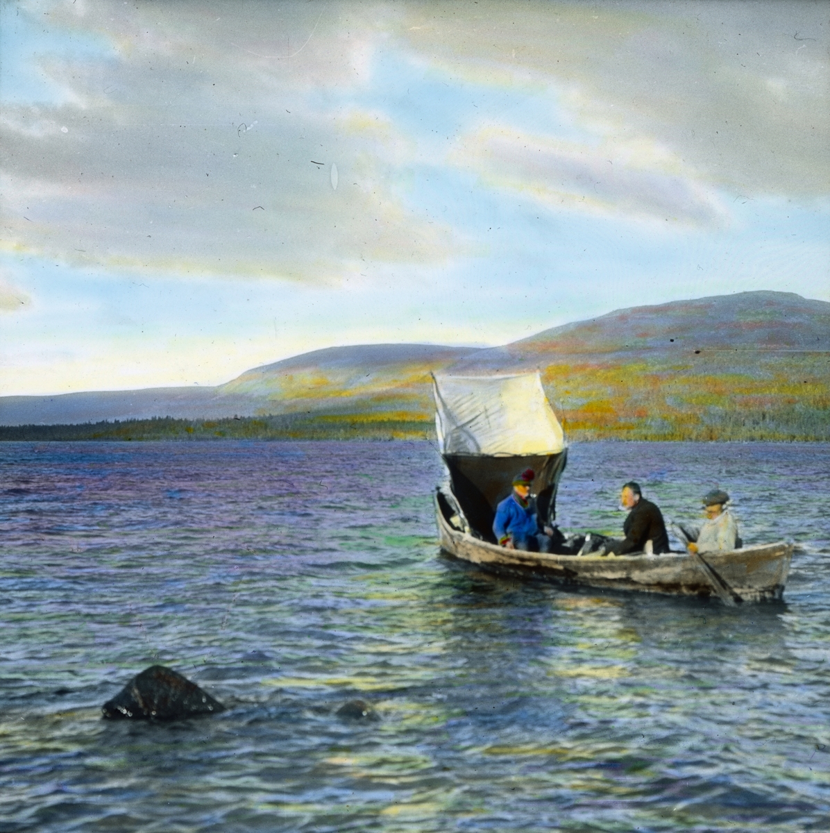 Håndkolorert dias. Tre menn ror i en trebåt på en innsjø. Båten har et enkelt seil forut.