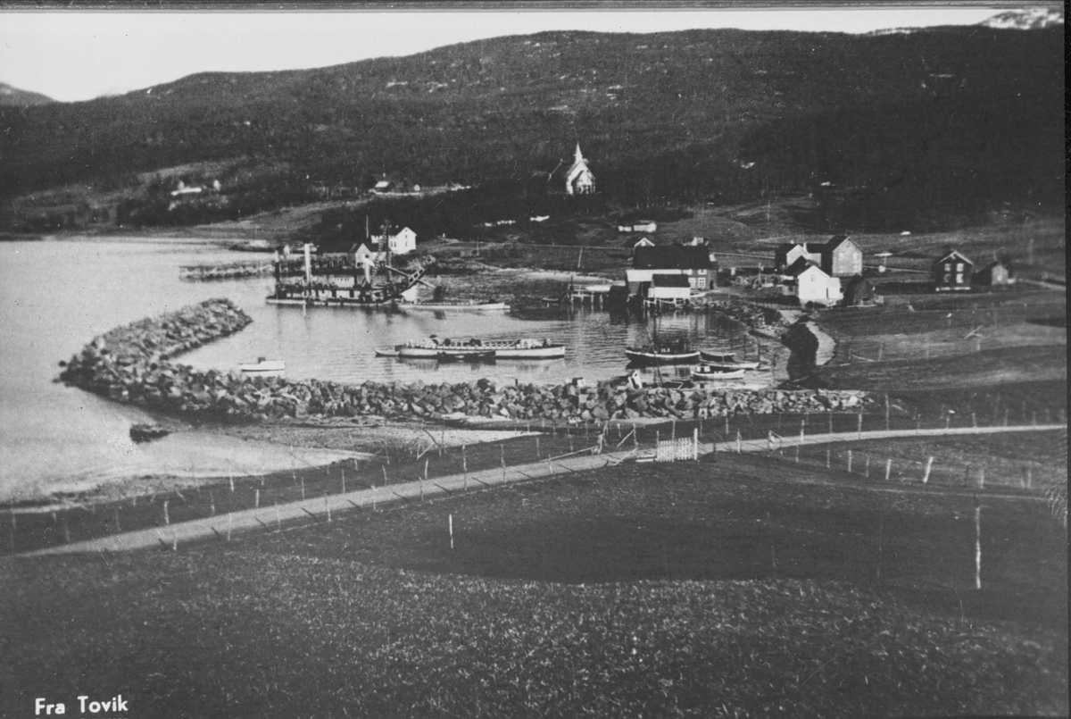 Bebyggelse og landskap rundt havna i Tovik. Moloen til venstre og kirka i bakgrunnen.