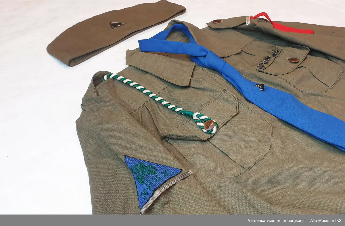 Speideruniform fra 1950-tallet komplett med jakke med påsydde stjerner og troppsnavn, skjørt, belte, snor til fløyte, lue med emblem, slips med emblem, håndbøker og sangbok.
