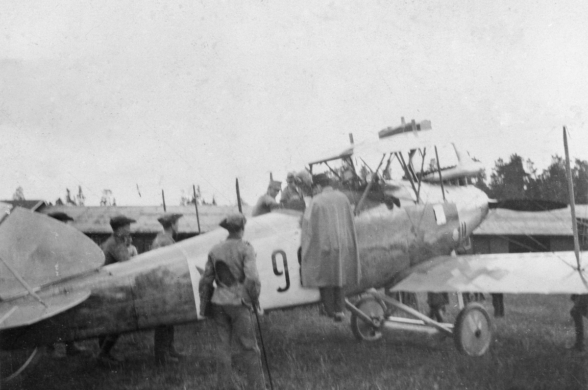 Militärer samlade vid flygplan FVM S 18 vid Flygkompaniets F-hangar på Malmen. Omkring 1919-1926. Vy snett bakifrån.