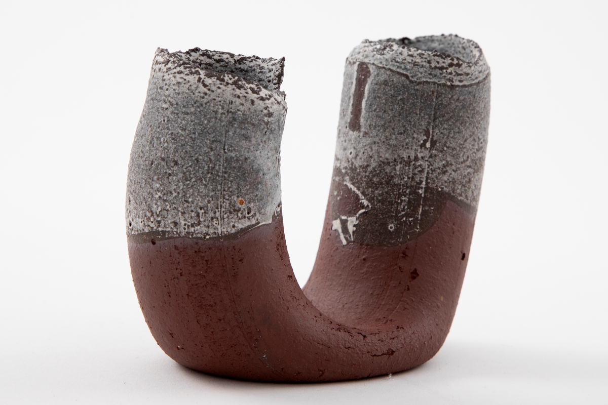 Vase i matt rødbrun terrakotta. U-form med riller og åpne ender med ruglete render. Hvit halvtransparent glasur på begge ender og på innsiden av munningene.