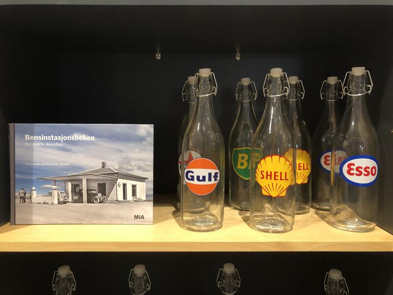 Flasker med bensinstasjonslogo og bok om bensinstasjoner, i museumsbutikken.
