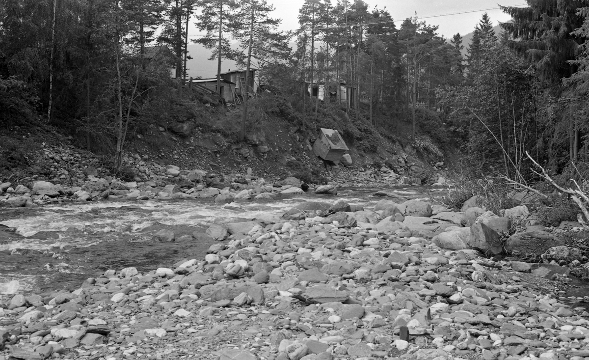 Fra elva Tromsa i Fåvang i Ringebu kommune i Gudbrandsdalen sommeren 1958, etter at dette vassdraget i pinsehelga, tidligere på sommeren, hadde vært utsatt for en sjeldent stor regnflom, som kom oppå det vassdrag der det allerede gikk mye smeltevann. Dette førte til store skader, både her oppe i elveløpet og i det nedenforliggende grendesenteret - se fanen «Opplysninger». På dette fotografiet, som er tatt i medstrøms retning - ser vi et betongstøpt lite hus med pulttak som hadde glidd ut i den bratte elveskråningen.

Topografien i Tromsas elveløp var meget kupert, og fra gammelt av ble det ikke fløtet tømmer der i det hele tatt. I 1958 var det imidlertid innmeldt 28 325 tømmerstokker til fløting i denne elva. De første stokkene ble utislått 28. mai, like etter flomkatastrofen. Med unntak av 169 stokker skal dette tømmeret ha nådd ned til Gudbrandsdalslågen.