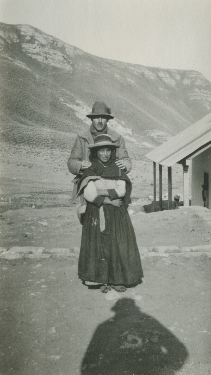 Fotografi från expedition till Peru 1920. Motiv av expeditionsdeltagare och kvinna utanför stuga i bergen.