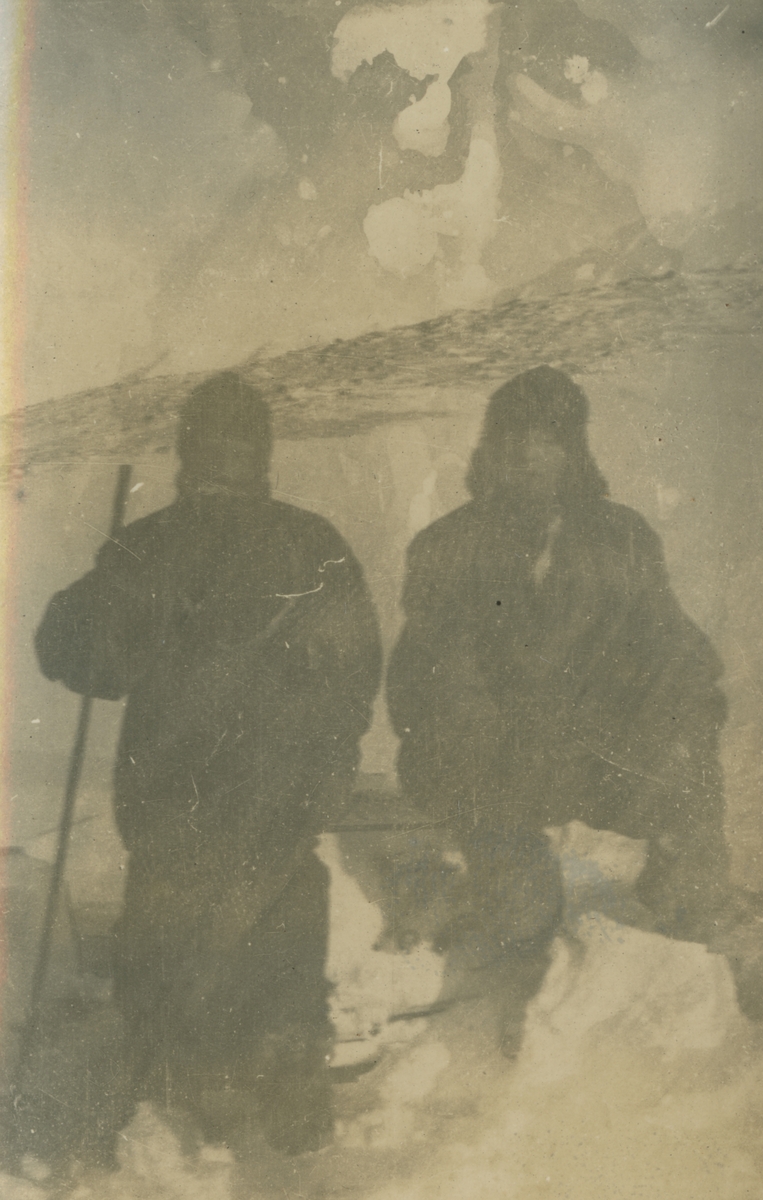 Fotografi från expedition till Spetsbergen. Motiv av två expeditionsdeltagare som sitter på ett snöblock i ett snö- och islandskap..
