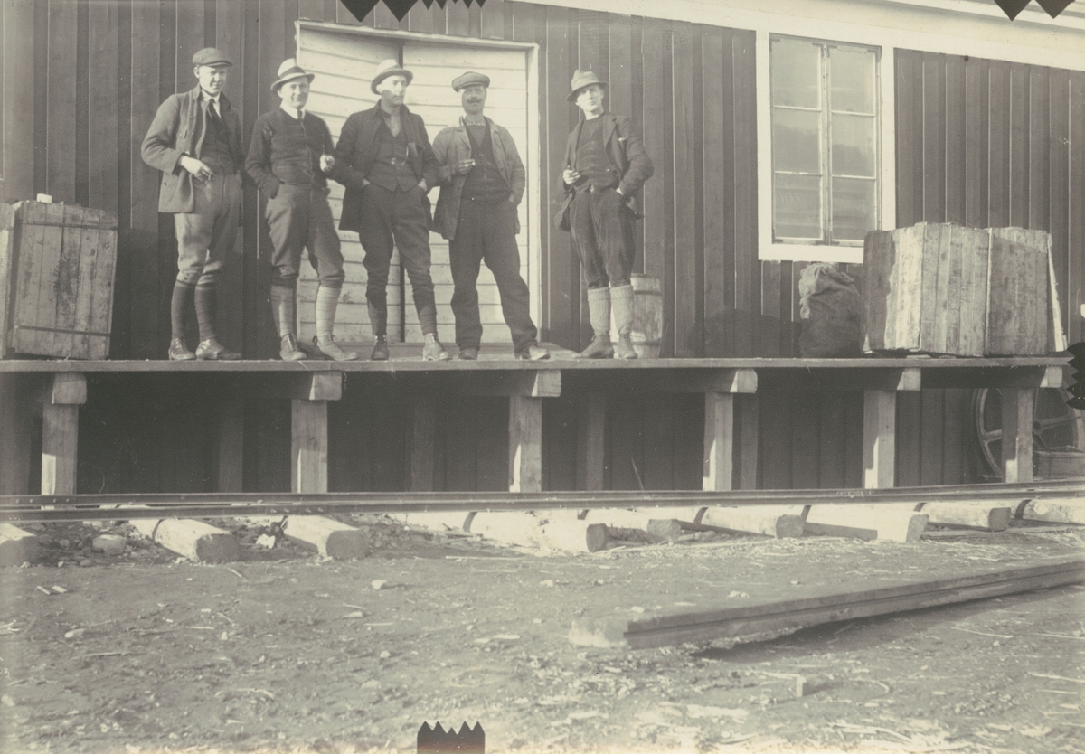 Fotografi från expedition till Spetsbergen 1920. Motiv av fem män utanför trähus.