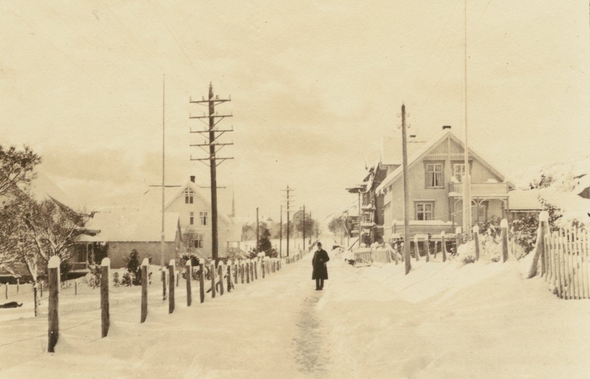 Fotografi från Albin Ahrenbergs resa till Grönland 1929. Motiv av man på snötäckt gata i liten stad.